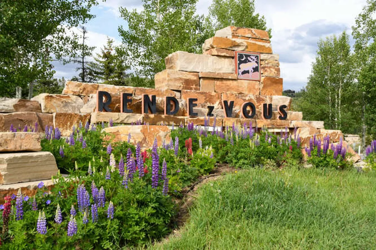 This image features an exterior scene with a welcoming stone sign surrounded by colorful flowers and lush green grass. The natural setting exudes freshness and highlights access to outdoor spaces, perfect for walks and play with pets.