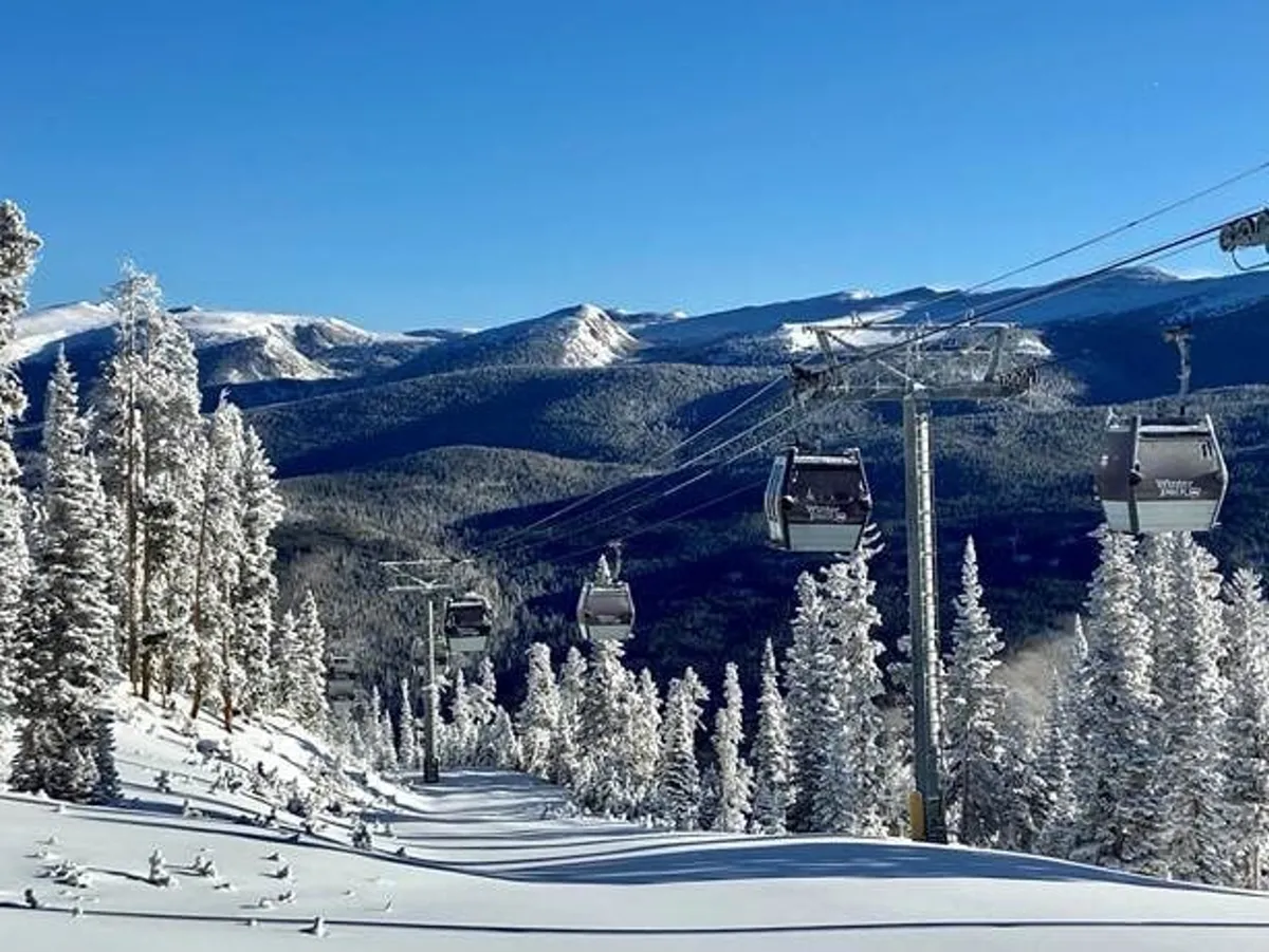 Ski lift gondolas glide above a snow-blanketed landscape with majestic mountains in the background and evergreen trees below. The setting radiates adventure and captures the essence of a true mountain resort.