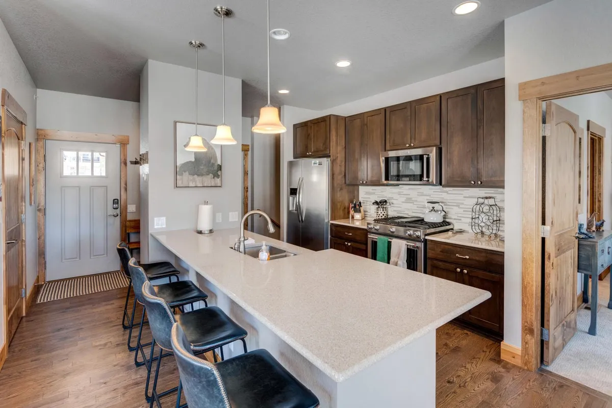 A bright and inviting kitchen featuring a large island with bar stools, sleek stainless steel appliances, custom cabinetry, and designer pendant lighting. The space feels open and perfect for both cooking and casual family gatherings, with clear sightlines for interaction while preparing meals.