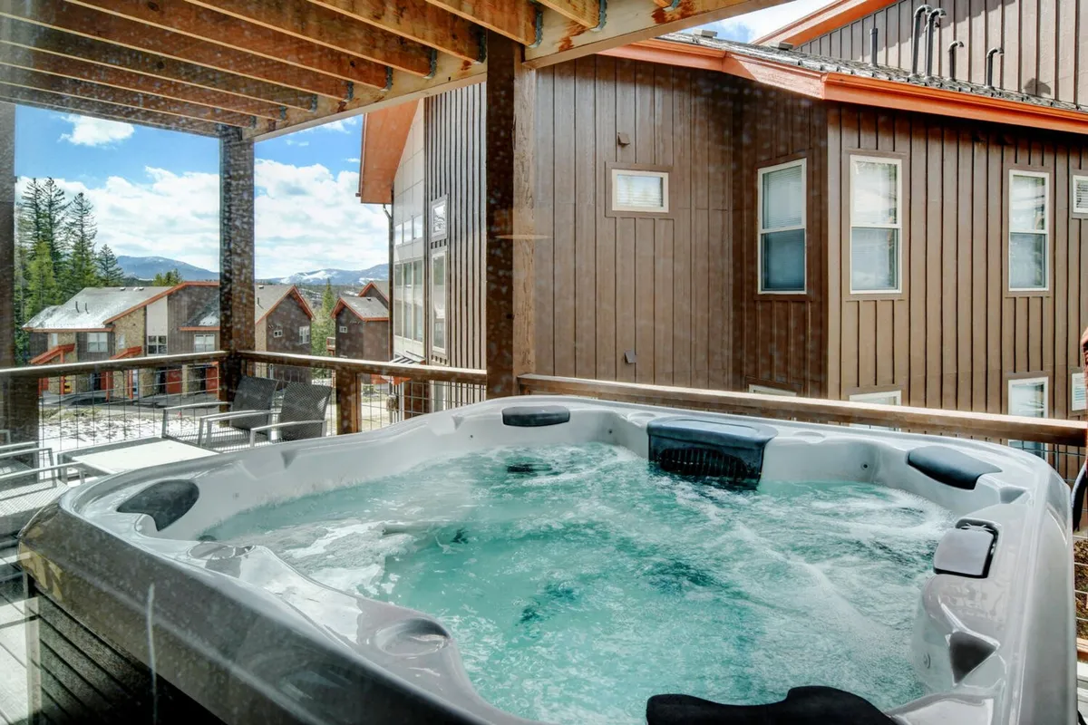 A serene hot tub area with wooden beams and a view of the surrounding landscape, hinting at relaxation after a day of adventure. Friends or family can be seen unwinding and enjoying scenic vistas from the hot tub.