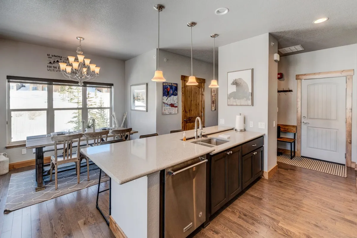 An open-concept kitchen and dining area with a central island, elegant dining table, contemporary chandelier, and large windows that frame beautiful outdoor views. The atmosphere is warm and inviting, perfect for both holiday feasts and quiet morning coffees.