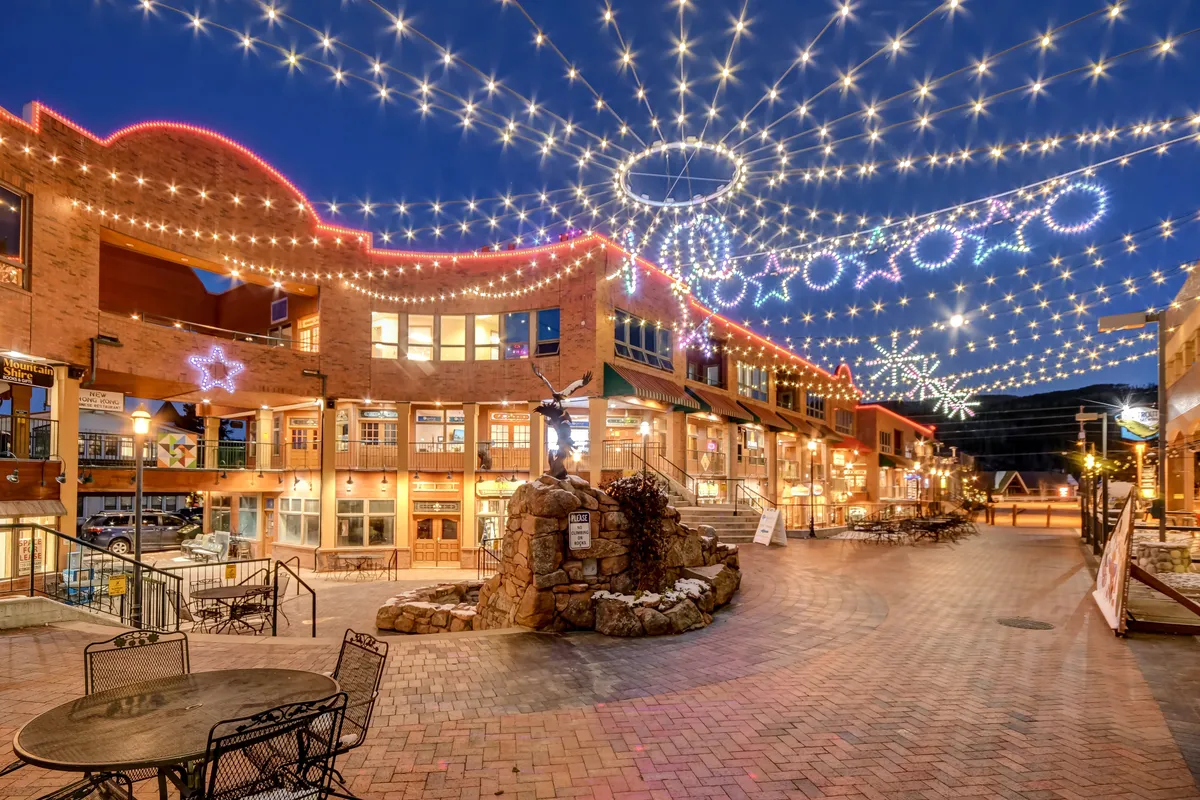 A vibrant streetscape with string lights overhead, decorative stars, a brick pathway, stone fountain, and boutique storefronts. The lively atmosphere is perfect for exploring shopping, dining, and local events.