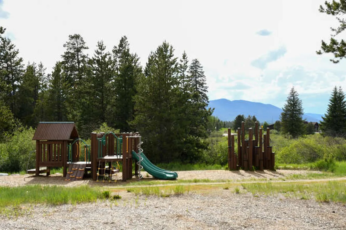 A cheerful playground scene featuring green slides and a tall wooden climbing structure, with children playing and families gathering for outdoor picnics and fun.