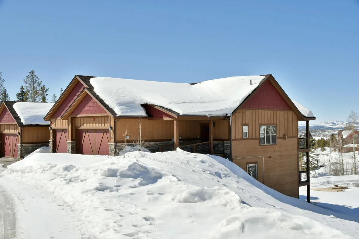 A snow-covered villa with warm wooden siding nestled among evergreen trees. The inviting exterior suggests cozy evenings inside, and the winter setting hints at proximity to mountain adventures and resort activities.